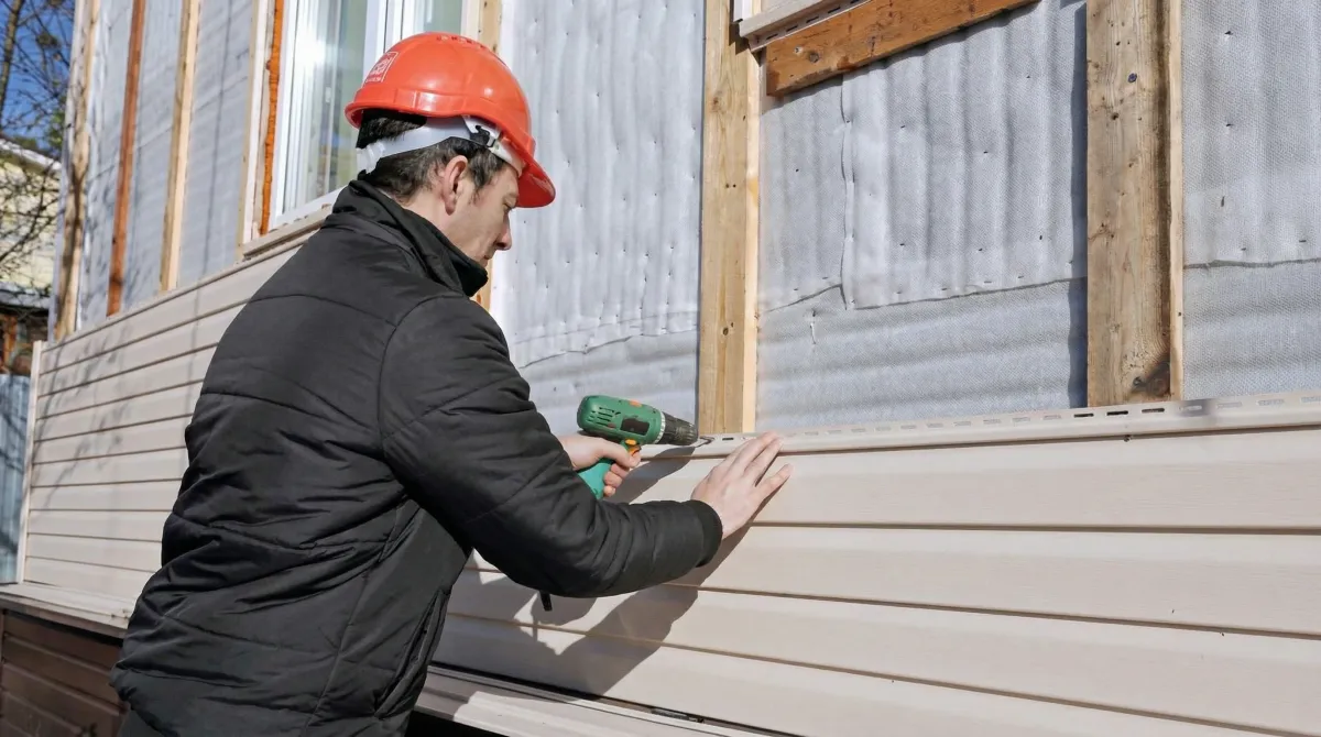 Siding replacement professional using a power drill to install new tan vinyl siding on a home exterior in Philadelphia, PA